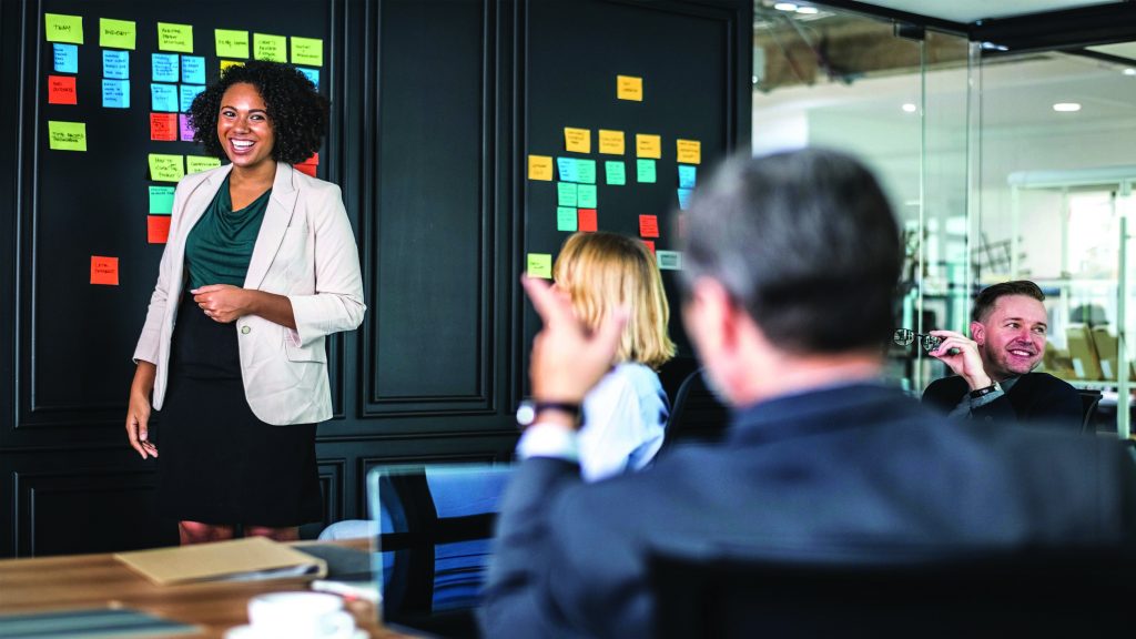 A focus group taking place for the Community Foundation of Ireland. A woman stands at the front of a room with post-its on the wall, a group of people looking on