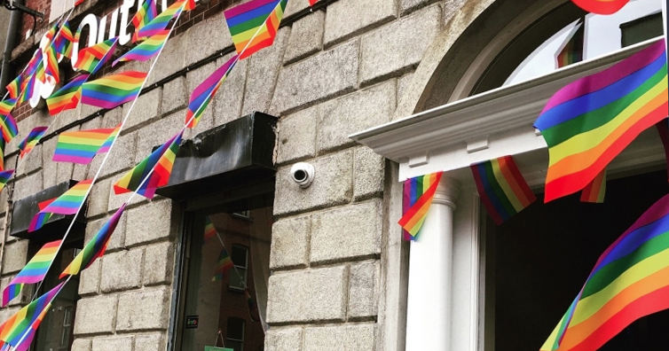 Image of Outhouse draped in rainbow flags.