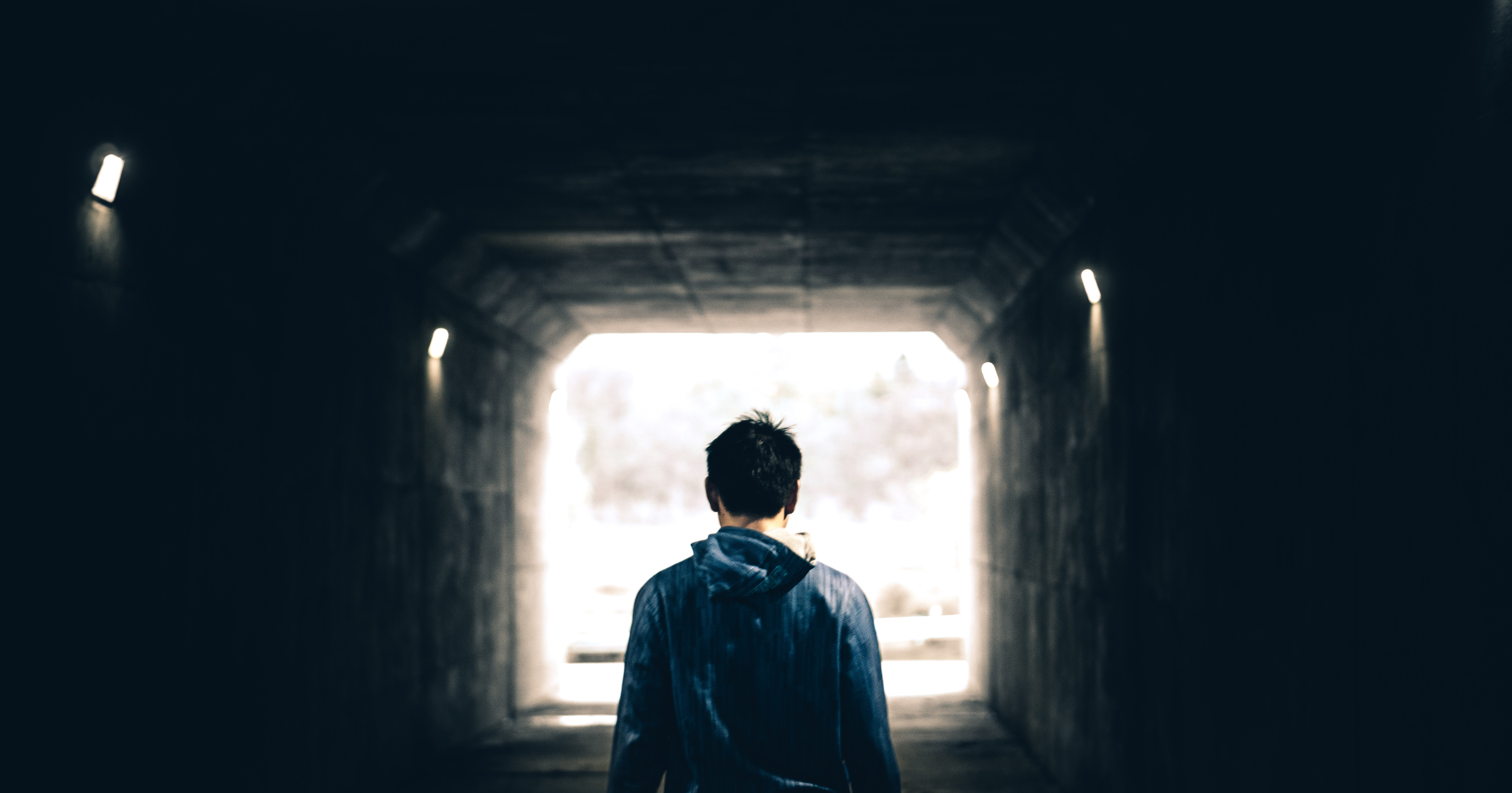 A teenagers seen from behind in a dark tunnel with light at the end