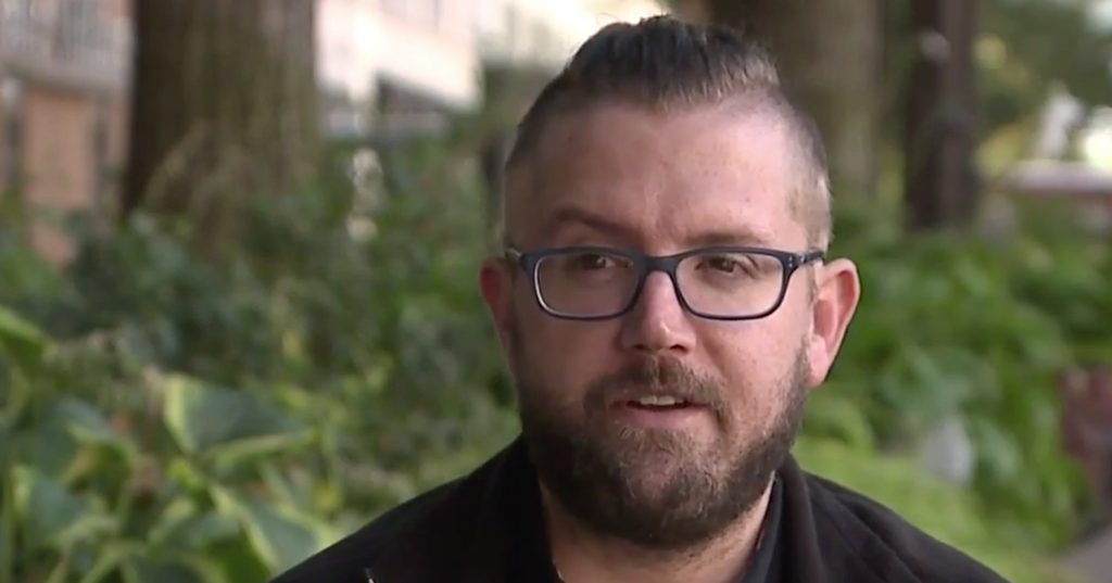 Minister Keith Kozak dressed in black and sitting outdoors, speaks to an interviewer off camera