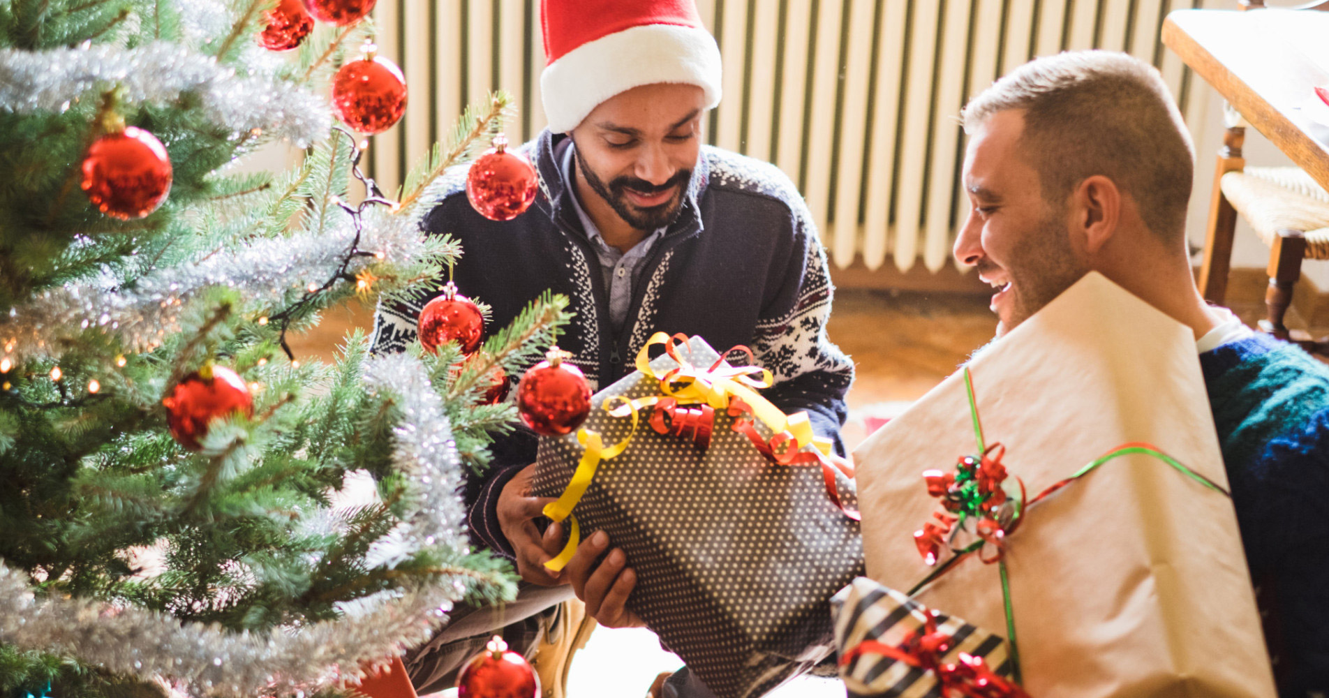 Gay couple celebrating Christmas by exchanging gifts by the Christmas tree