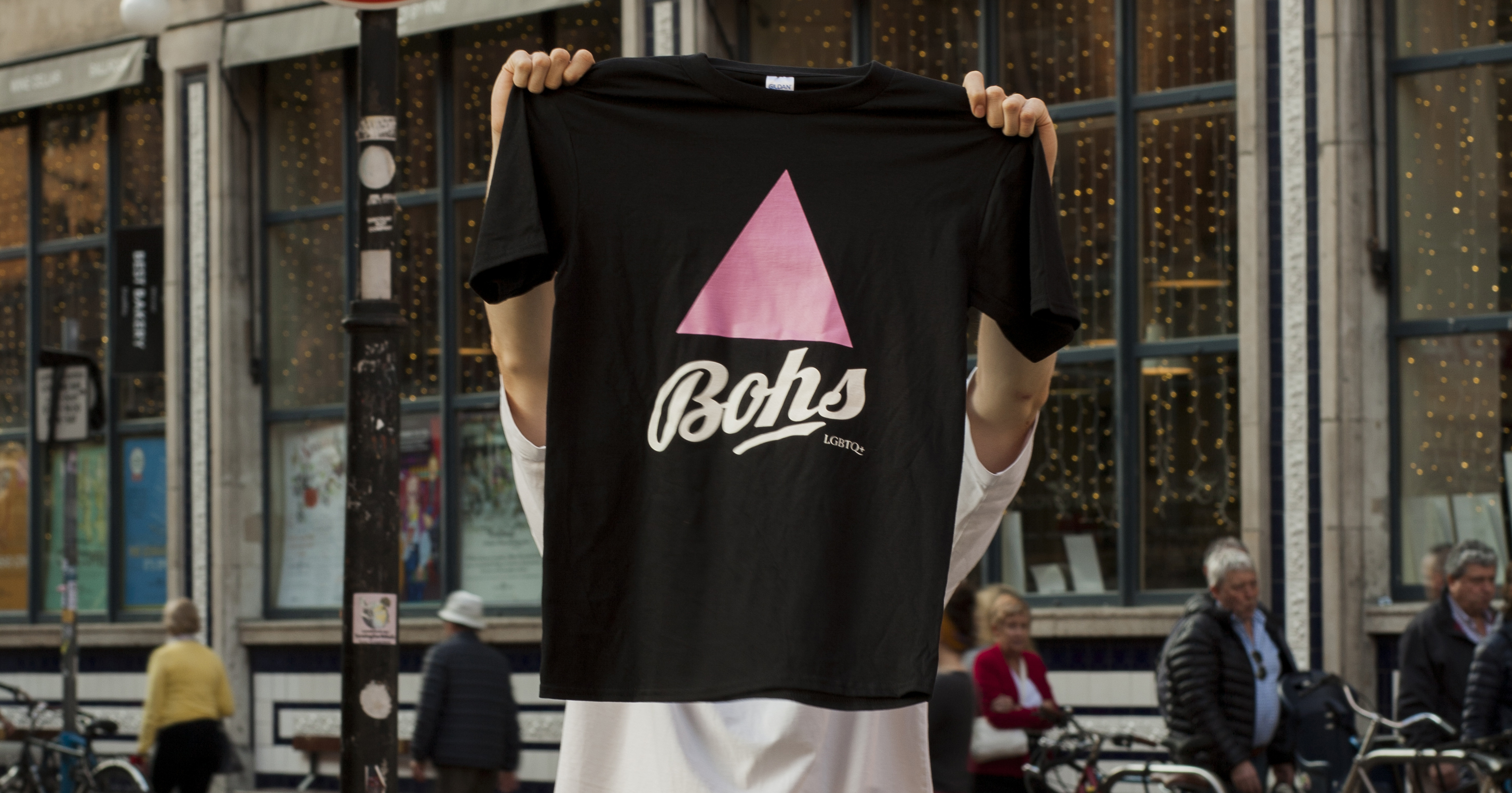A person on the street holding up t-shirt fan wear with a pink triangle and the Bohemians club logo