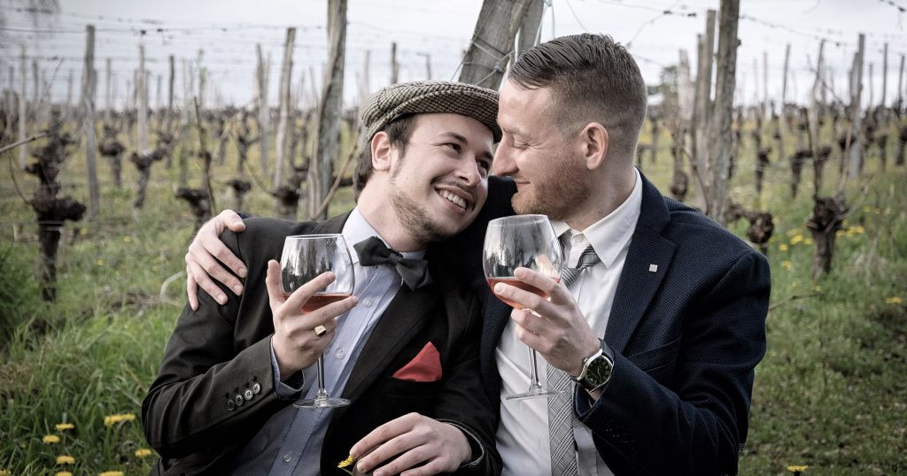 A gay couple rinking wine on their honeymoon in Ireland, looking into each other's eyes.