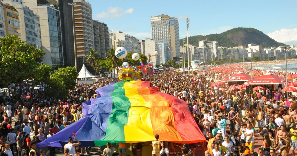 Hundreds of Brazilians on the beach in Rio carrying a huge Pride flag