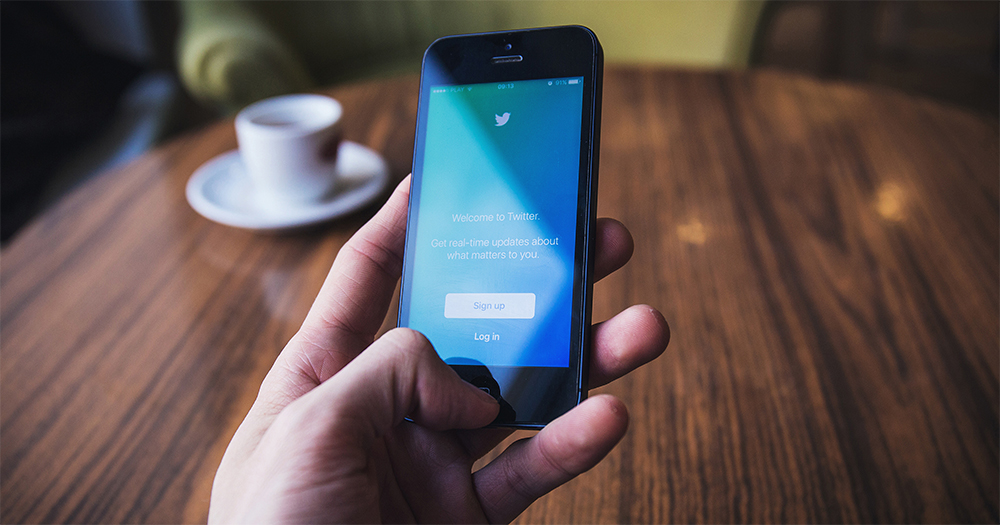A hand in close up holds an iPhone with The Twitter logo on the screen as Twitter bans transphobic content