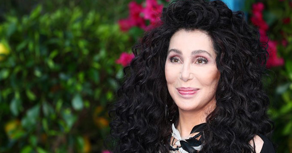 Cher standing in front of a bush.