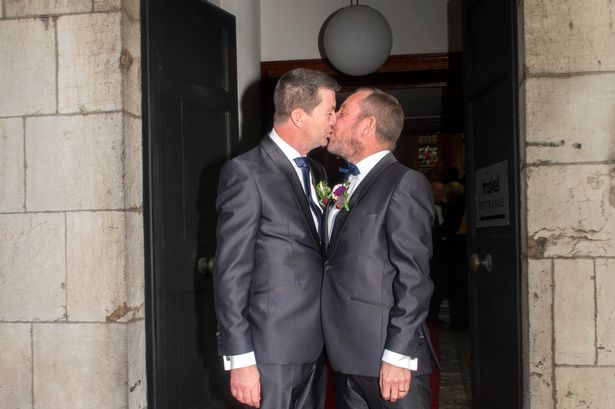 TD Jerry Buttimer at his wedding to his husband, kissing him in front of the door to the venue.
