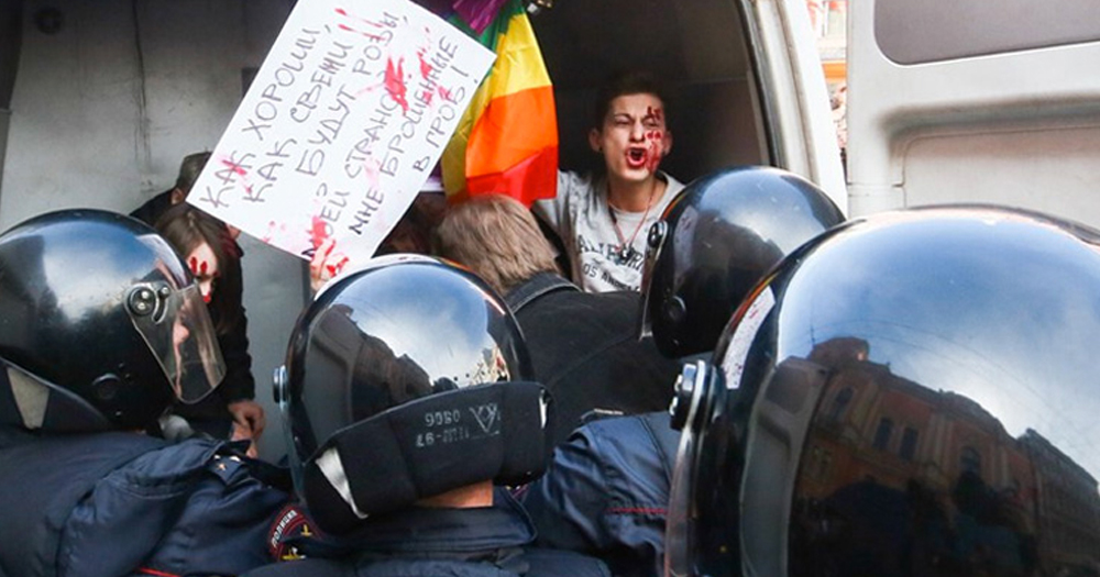 Chechen authorities force a protestor carrying a rainbow flag into the back of a van.