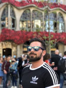 A young man with a beard wearing sunglasses in Barcelona as part of a postcards home feature