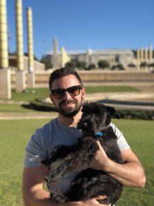 A young man with a beard holding a dog in Barcelona as part of a postcards home feature