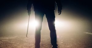 A person holds a weapon in front of a car.