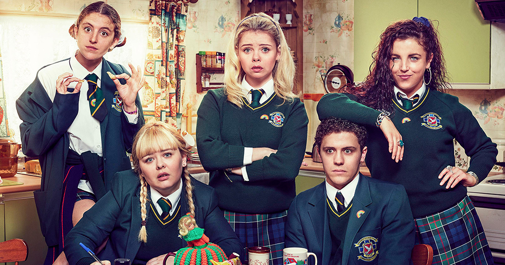 The five lead characters from Derry Girls all dressed in school uniforms pose comedically around a kitchen table