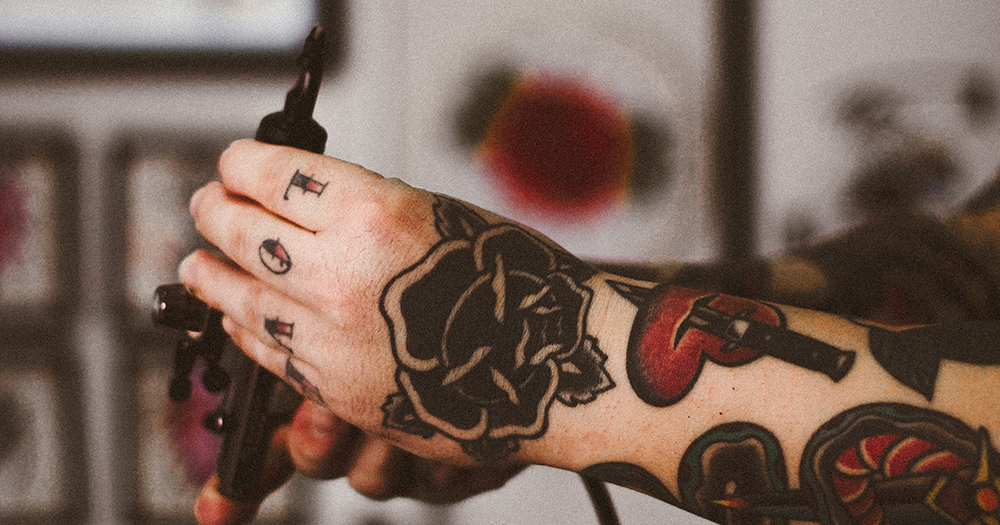 A tattoo artist with tattoos of hearts and the word "love" holding a tattoo gun