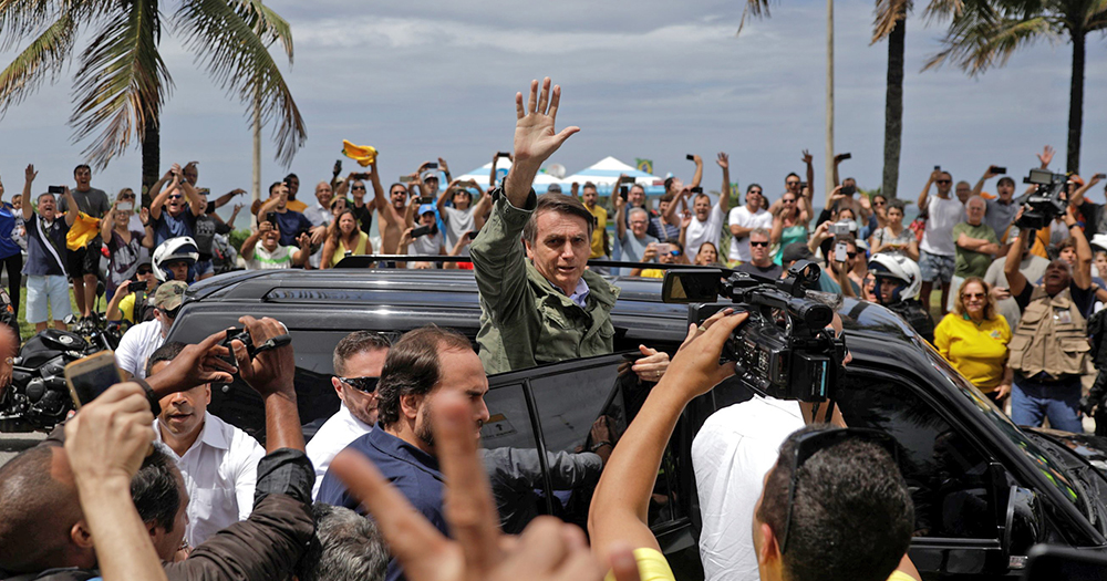 Jair Bolsonaro waves to supporters while leaning out of his car