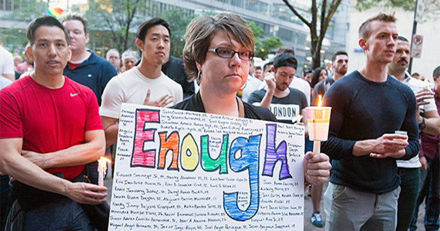 People at a vigil, a woman is holding a sign which reads "Enough", demanding demanding hate crime legislation