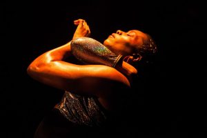 In a promo for Nightclubbing, a woman on a dark stage lit from above, hugs her arm around her neck