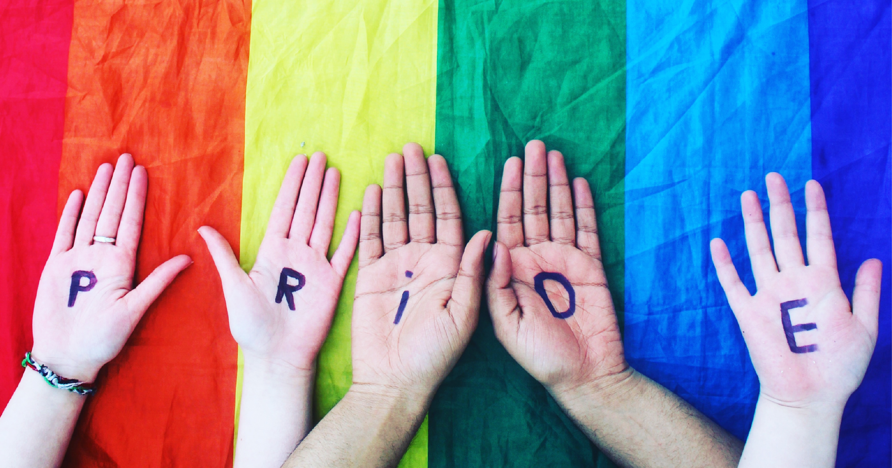 A rainbow flag and 5 hands. Each hand contains a letter from the word PRIDE. This is the cover of the new magazine GLUEPOT