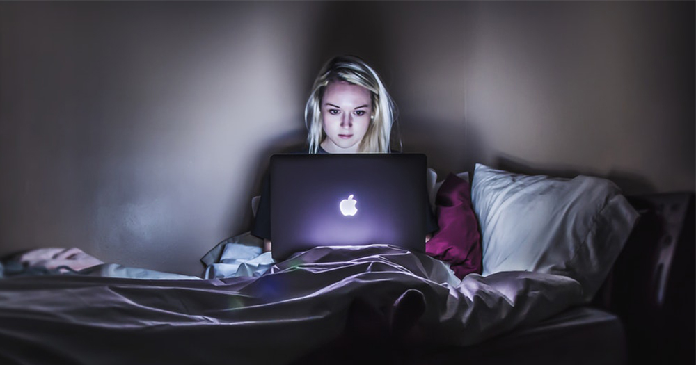Girl sitting on her bed, browsing the internet on a macbook. In this story a young woman talks about how the bisexual online community helped her