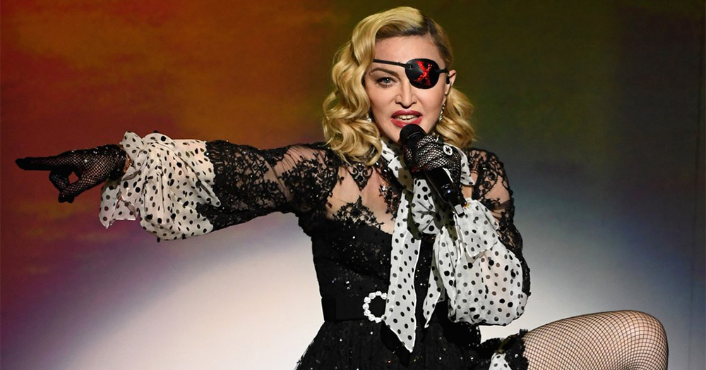 Pop star Madonna performing on stage, wearing an eyepatch and pointing to her right