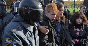 Helmeted policemen with covered faces march a gay male couple and their female friend away.