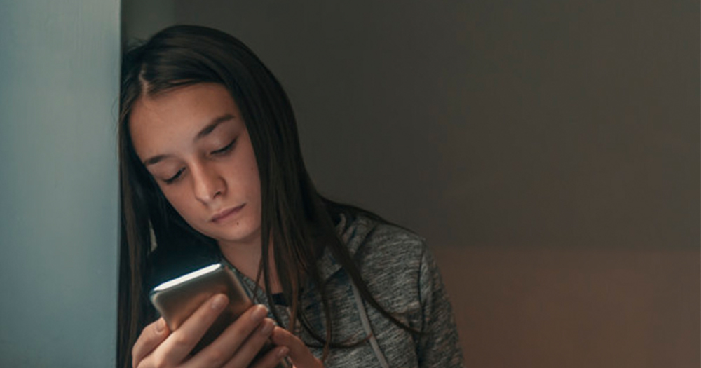 sad teenager looking at phone in the dark