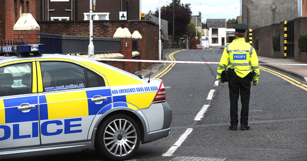 Police Man stands beside police car in Northern Ireland