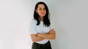 a young woman with folded arms standing in front of a white background.