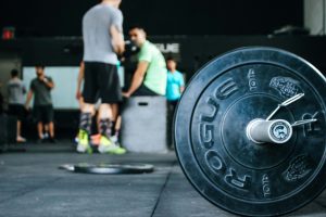 A barbell in the foreground, in the back of the gym, a group of men gather