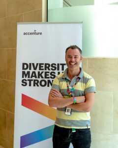 A smiling man stands beside a sign which reads 'diversity makes us stronger'
