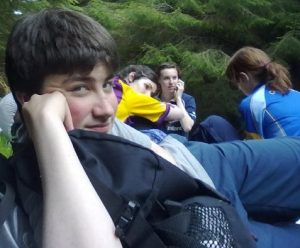A teenager in rural Ireland lying back on his elbow looking at the camera, a group of young people in the background.
