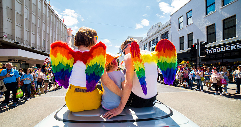 moms in angel wings sit on pride parade car with son