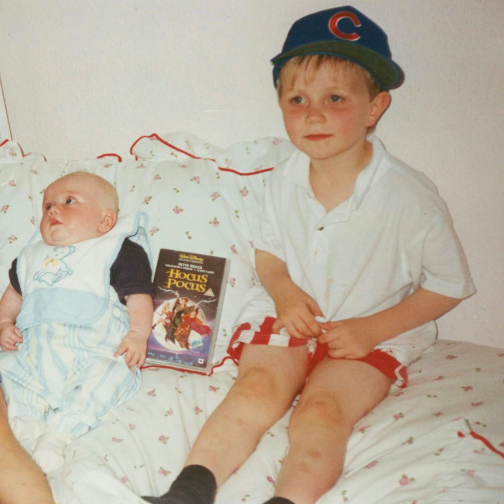 Family photo of a new born baby on a bed, his brother beside him. A VHS tape between them