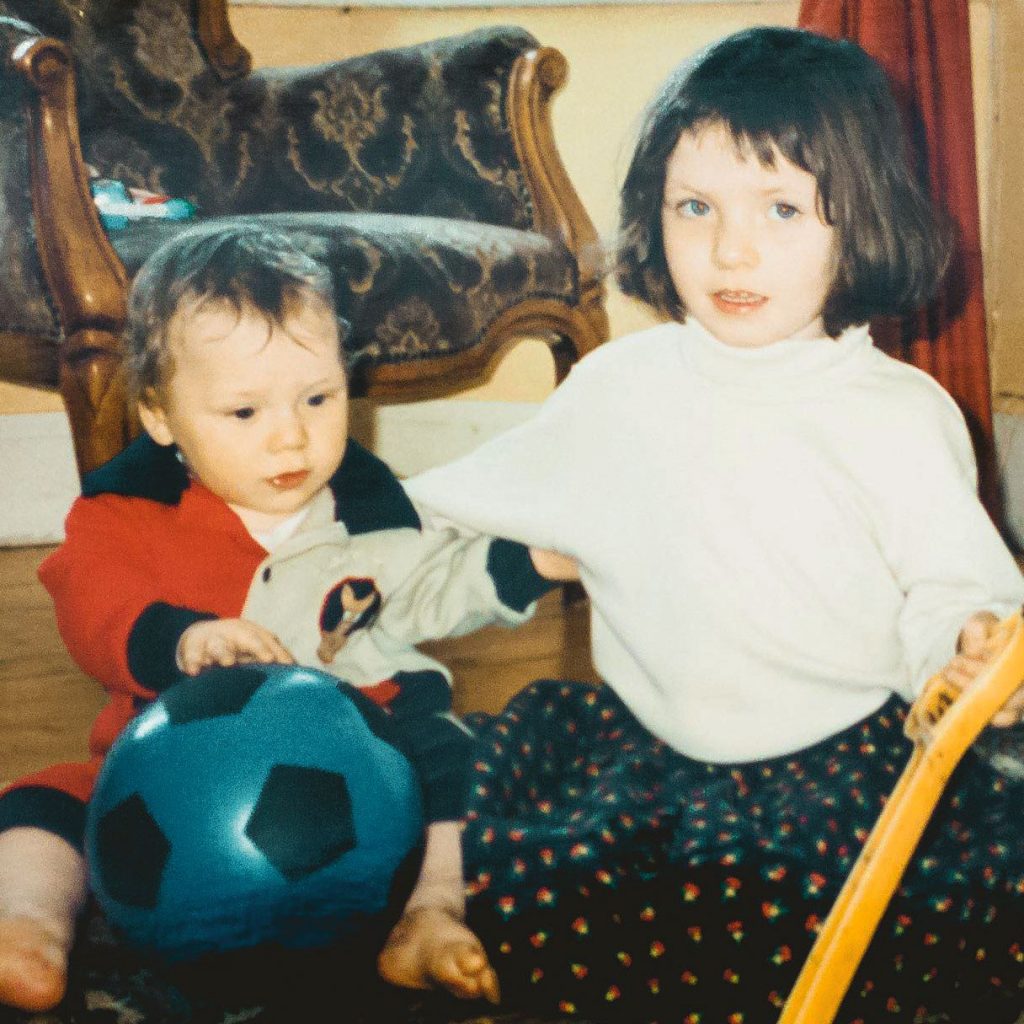 Family photo: a toddler holding a football and a little girl with a guitar, both sitting on the ground