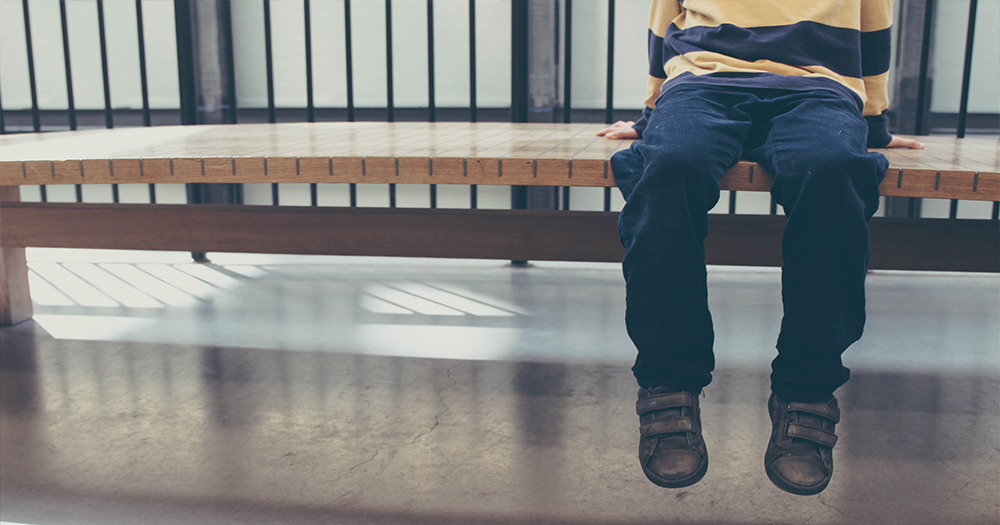 A child sitting on a bench with their feet hanging down