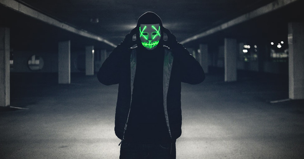 A person wearing Saw like a neon mask in an underground parking lot.