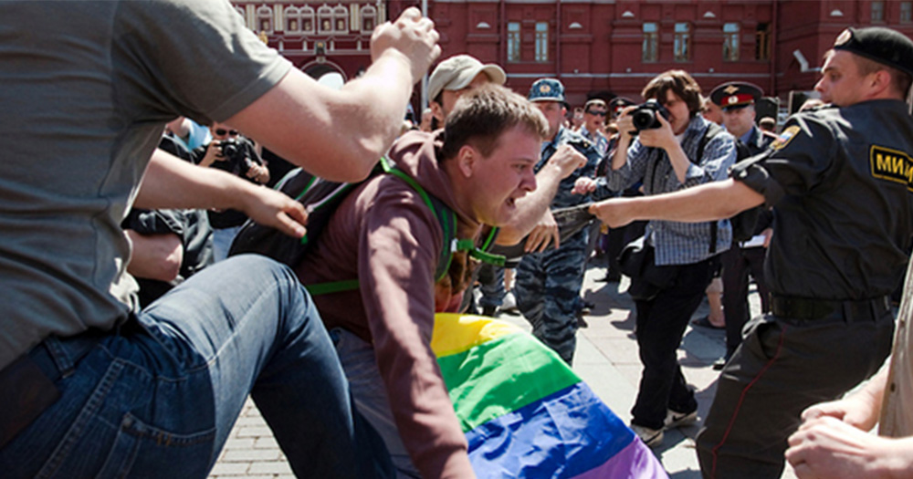 Man holding rainbow flag falling forward as Russia police looks ready to attack.