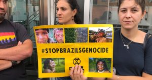 Woman holding a sign saying hshtag Stop Brazils Genocide as part of Extinction Rebellion protest