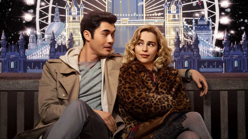 Stars of upcoming festive film Last Christmas Emilia Clarke and Henry Golding sitting on a bench in front of a winter London scene