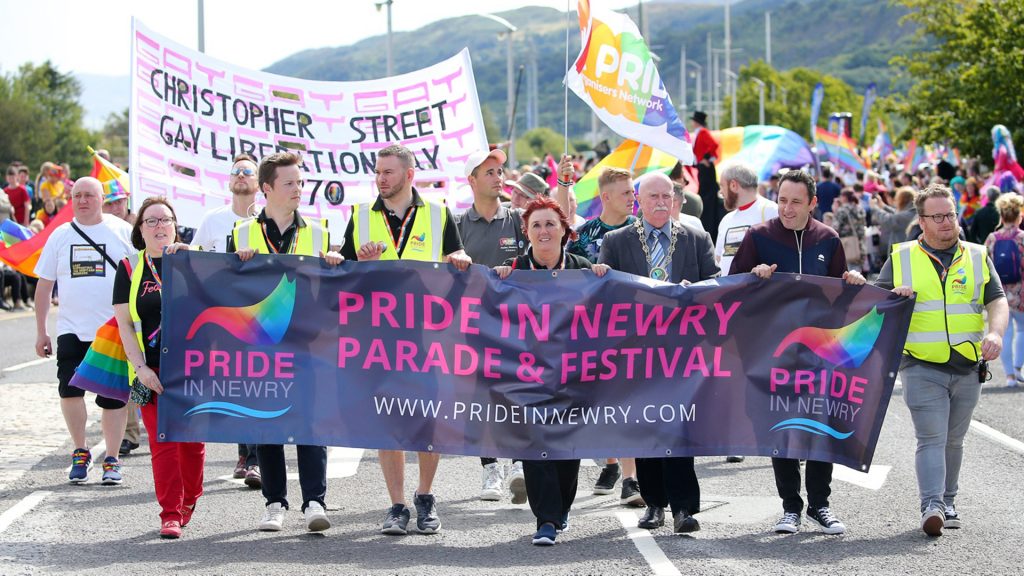 Newry Pride festival organisers walking in parade holding a banner which reads " Pride in Newry. Parade and festival"