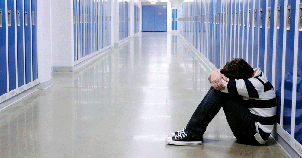 A child sitting in a school corridor , his head between his legs. Homophobic and transphobic bullying is still a major issue in schools.