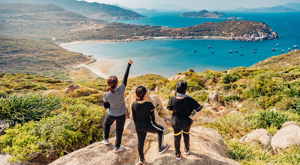 Three women standing on top of a mountain overlooking scenic lake, QuestionMark recently conducted a survey on LGBT+ travelling.