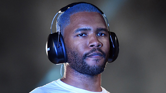 Frank Ocean wearing a white t-shirt and headphones. Ocean is one of the most revolutionary singers of his day.