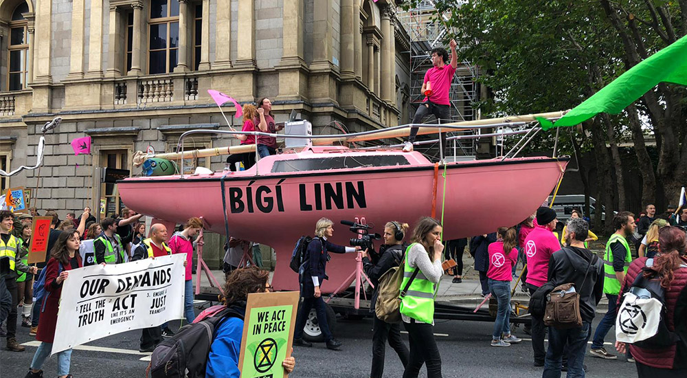 Image of a large pink boat saying Bigi Linn on the side, heading a protest walking down a street by the Dail.