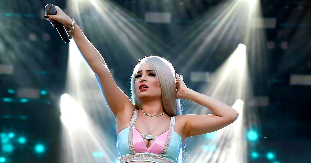 Pop singer Kim Petras during a live performance, holding the mic to the crowd