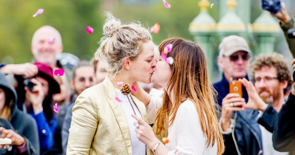 Wedding at Extinction Rebellion demonstration: Two women kissing while the crowd cheers behind them and rose petals are thrown in the air.