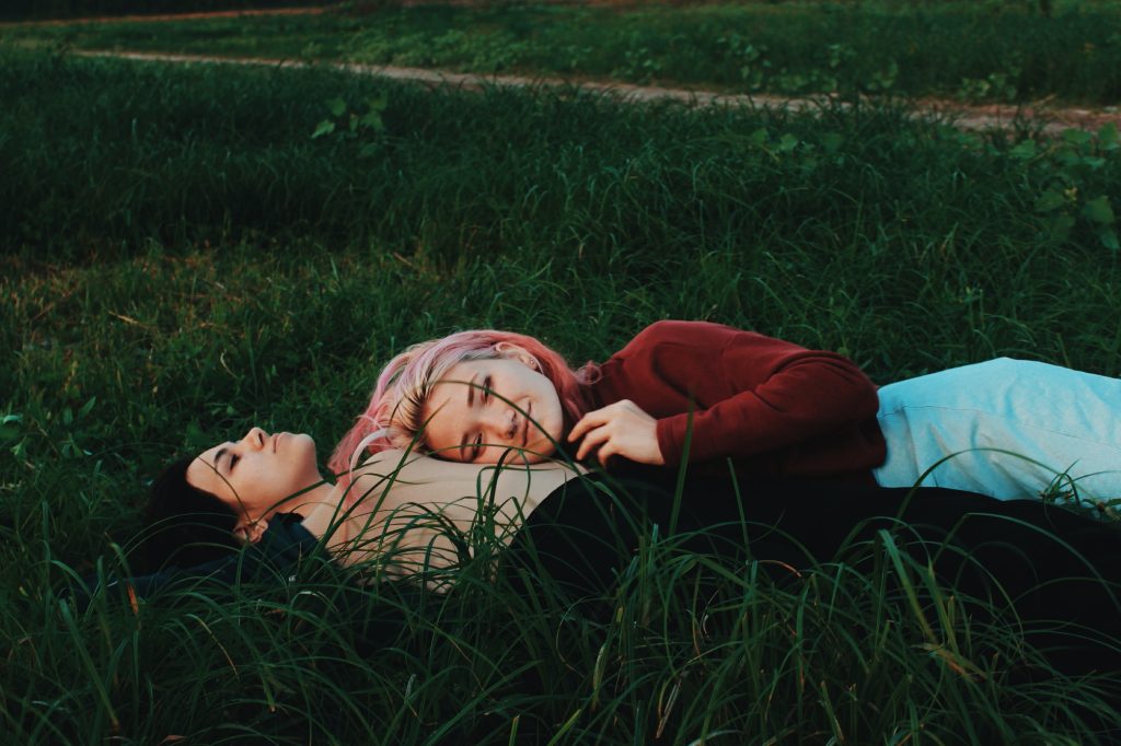 Two girls hugging and lying on the grass. This article is about mental health.
