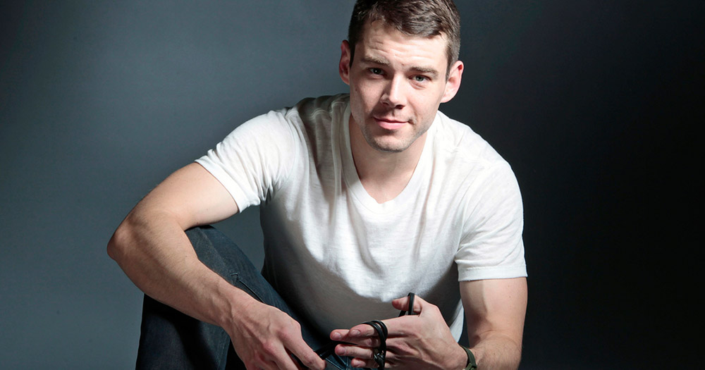 Brian J Smith sitting on the ground with rope around his fingers.