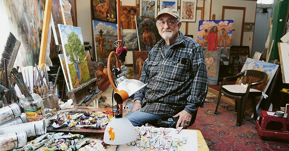 Artist Delmas Howe sitting in his studio, surrounded by his paintings