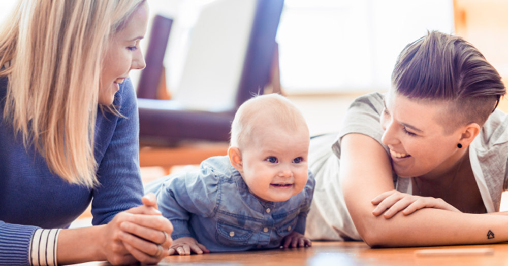 Lesbian couple lying on floor and laughing with a baby. As part of a new clinic programme, female same-sex parents can avail of "shared motherhood" fertility treatment"