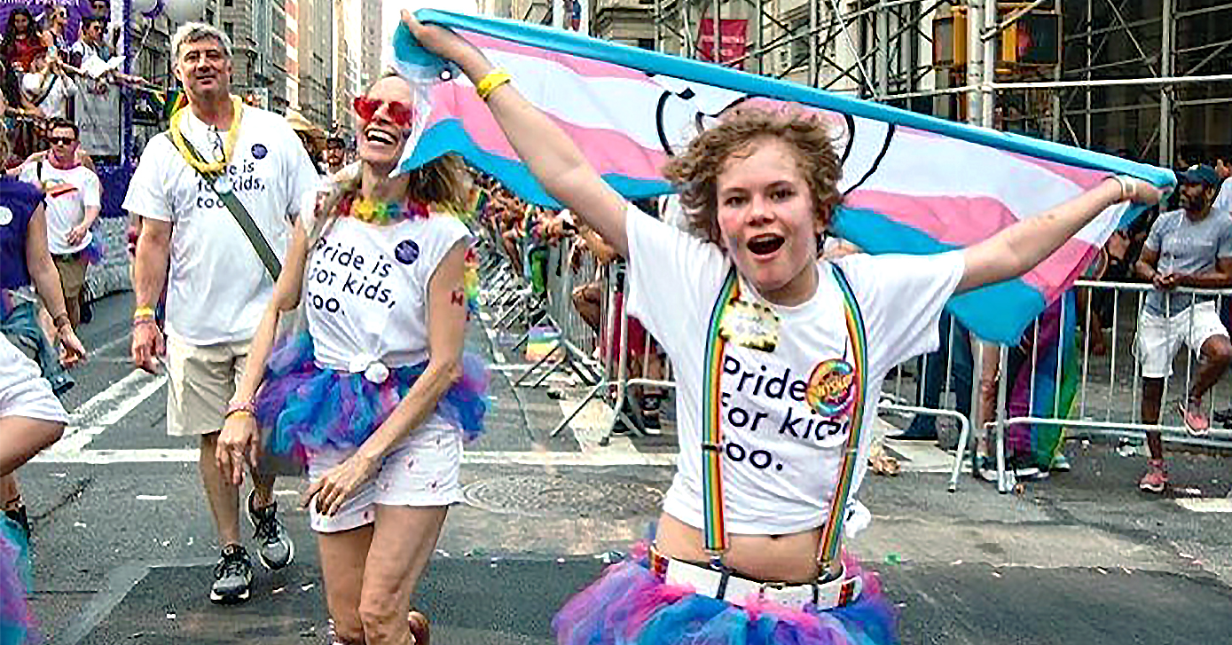A person holding a trans flag and smiling while walking down street.